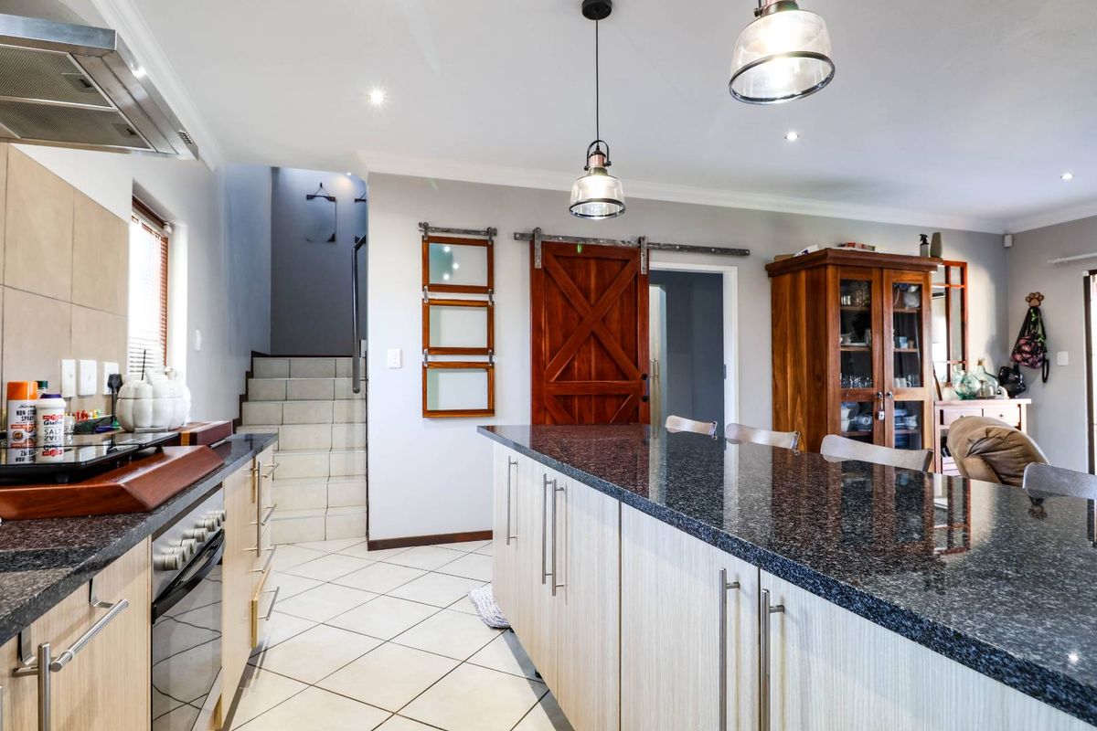 Modern kitchen featuring granite countertops, built-in oven, extractor fan, and a distinctive sliding barn door, with an open-plan layout leading to a staircase.