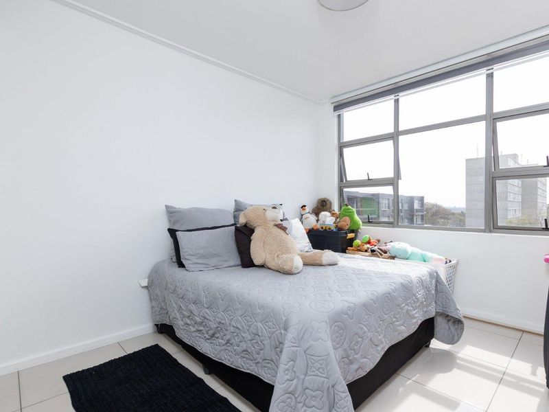 A bright bedroom featuring large aluminium-framed windows that provide ample natural light and tiled flooring throughout.