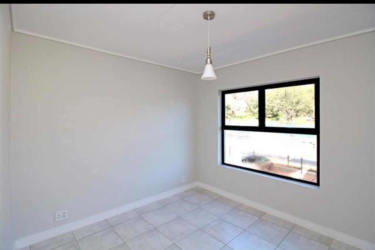 A bright, empty bedroom featuring neutral wall paint, tiled flooring, and a large window with a black frame.