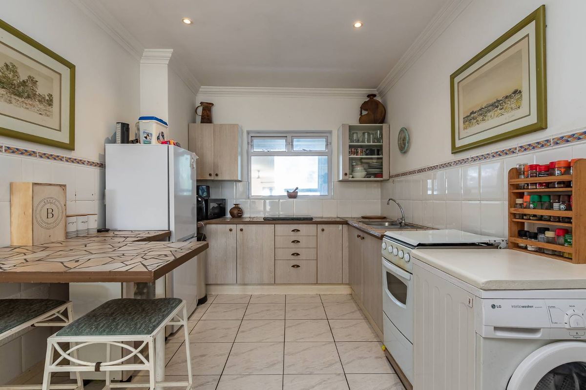 A functional kitchen featuring light wood-finish cabinetry, tiled countertops, ceramic floor tiles, and a tiled backsplash with decorative border accents.