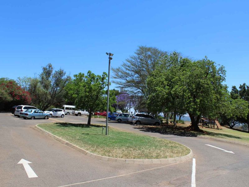 A view of the apartment complex parking area featuring paved driveways, landscaped green spaces, and mature trees.