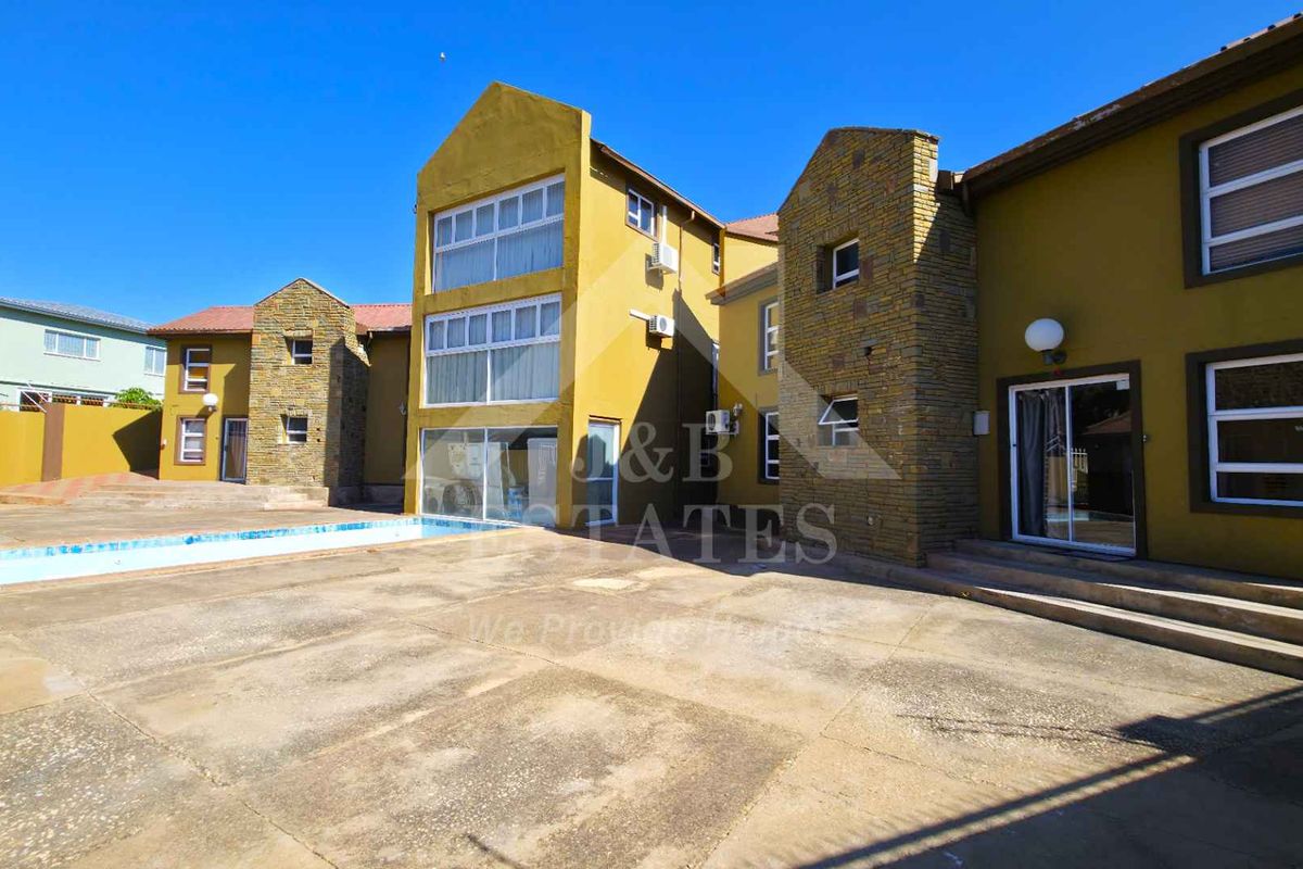 Rear exterior view of the property featuring a swimming pool, concrete patio area, and multi-story building facade with stone accents.