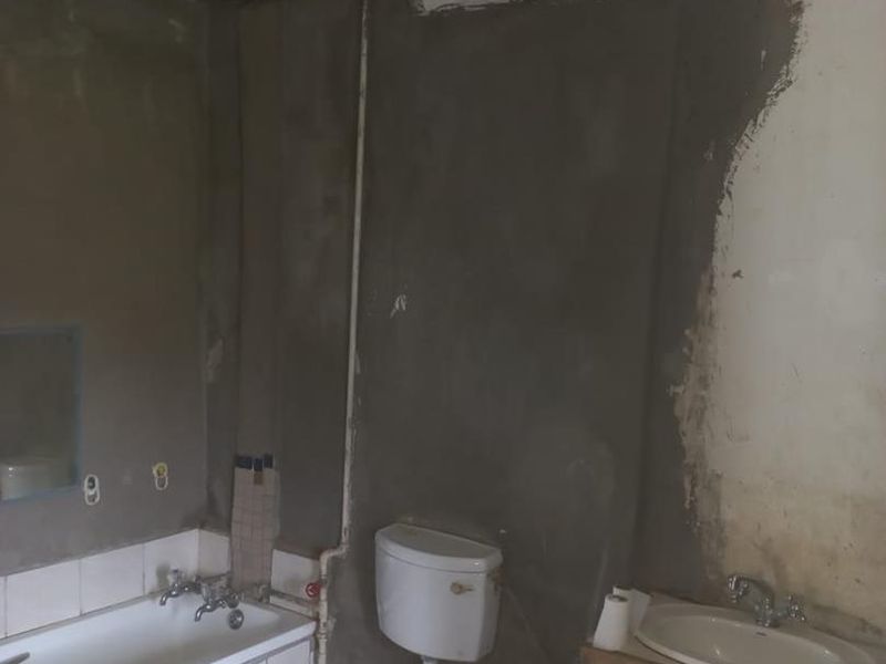 A bathroom in need of significant renovation, featuring a bathtub, toilet, and vanity basin with unfinished wall surfaces and exposed plumbing.