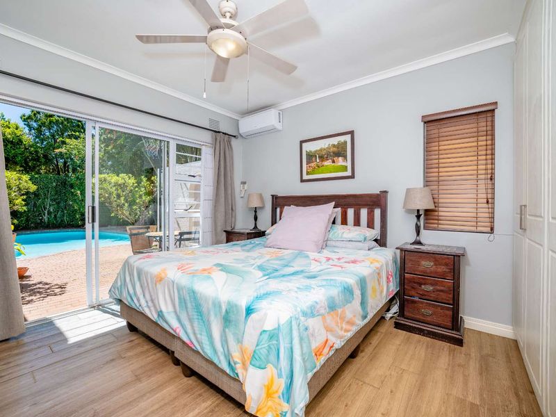 Well-maintained bedroom featuring timber-look flooring, built-in wardrobes, a ceiling fan, and direct access to the pool area through sliding glass doors.