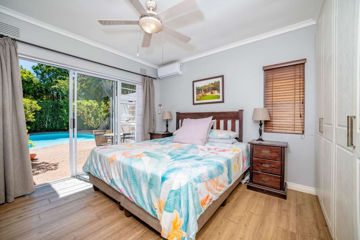 Well-maintained bedroom featuring timber-look flooring, built-in wardrobes, a ceiling fan, and direct access to the pool area through sliding glass doors.