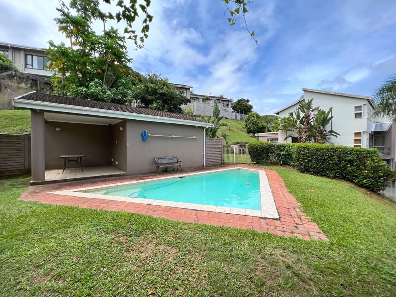 Outdoor pool area featuring a swimming pool with brick coping and an adjacent covered patio space set within a landscaped garden.