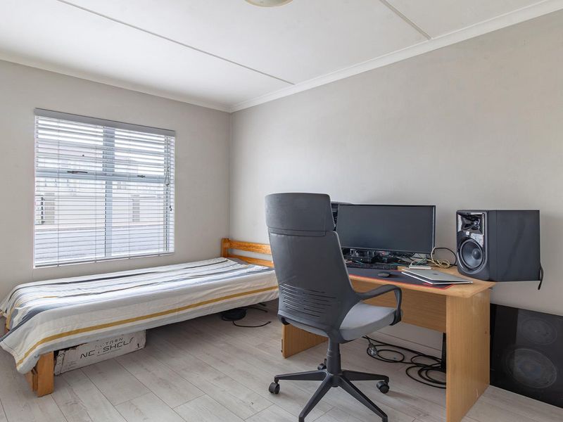 A functional bedroom featuring light-toned laminate flooring, neutral wall finishes, and a window fitted with venetian blinds.