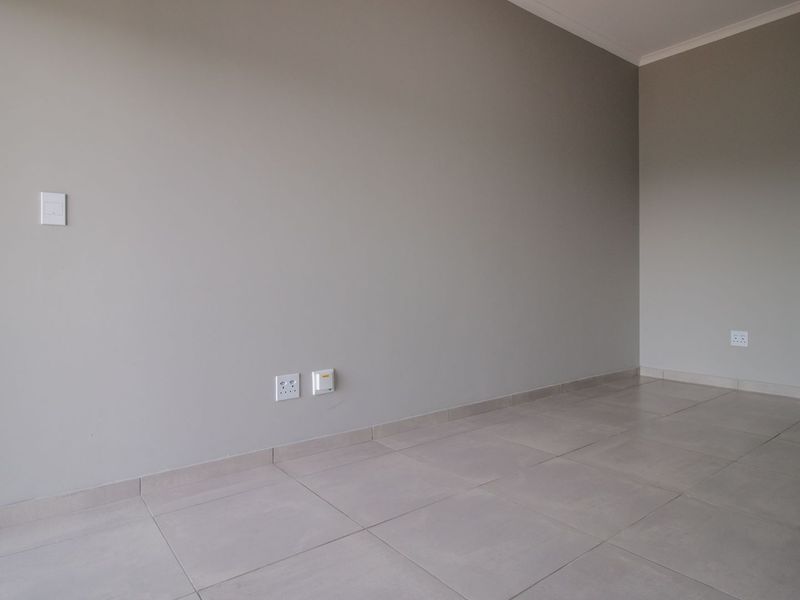A bright, empty living area featuring neutral wall tones and clean tiled flooring, providing a versatile blank canvas for interior design.