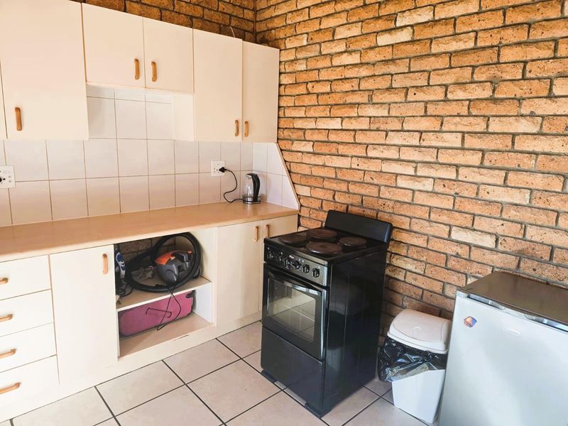A kitchen area featuring exposed brick walls, tiled flooring, built-in cabinetry with a tiled backsplash, and a freestanding stove.