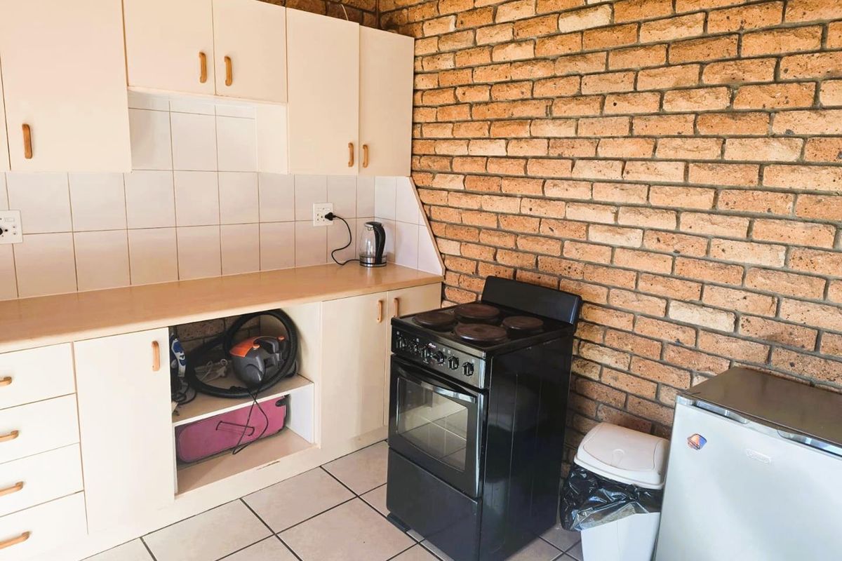 A kitchen area featuring exposed brick walls, tiled flooring, built-in cabinetry with a tiled backsplash, and a freestanding stove.