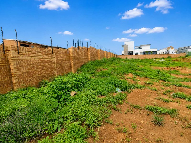A vacant residential plot featuring a secure brick perimeter wall with installed electric fencing, ready for development.