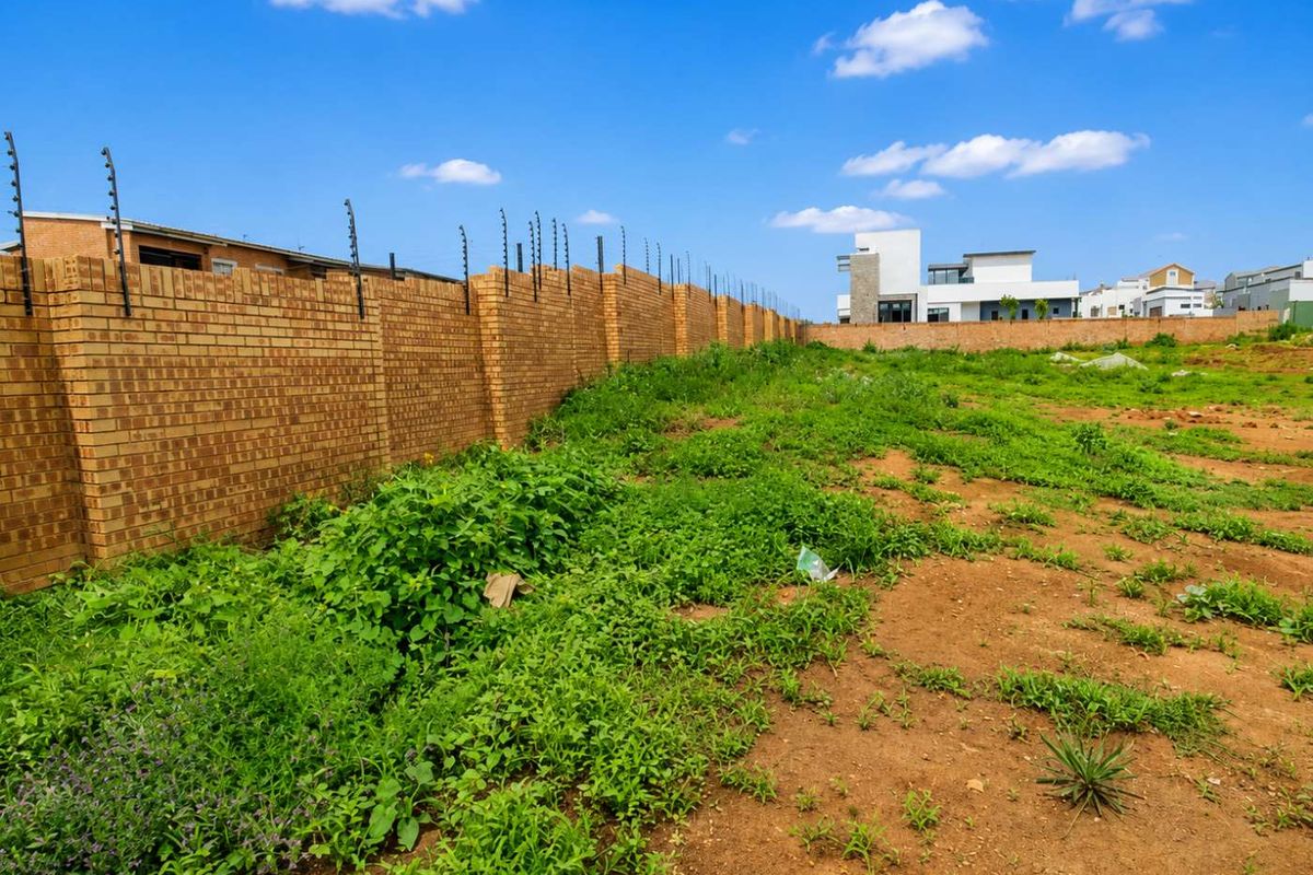A vacant residential plot featuring a secure brick perimeter wall with installed electric fencing, ready for development.