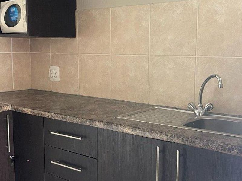 A functional kitchen area featuring dark cabinetry, laminate countertops, a stainless steel sink, and neutral tiled backsplash.