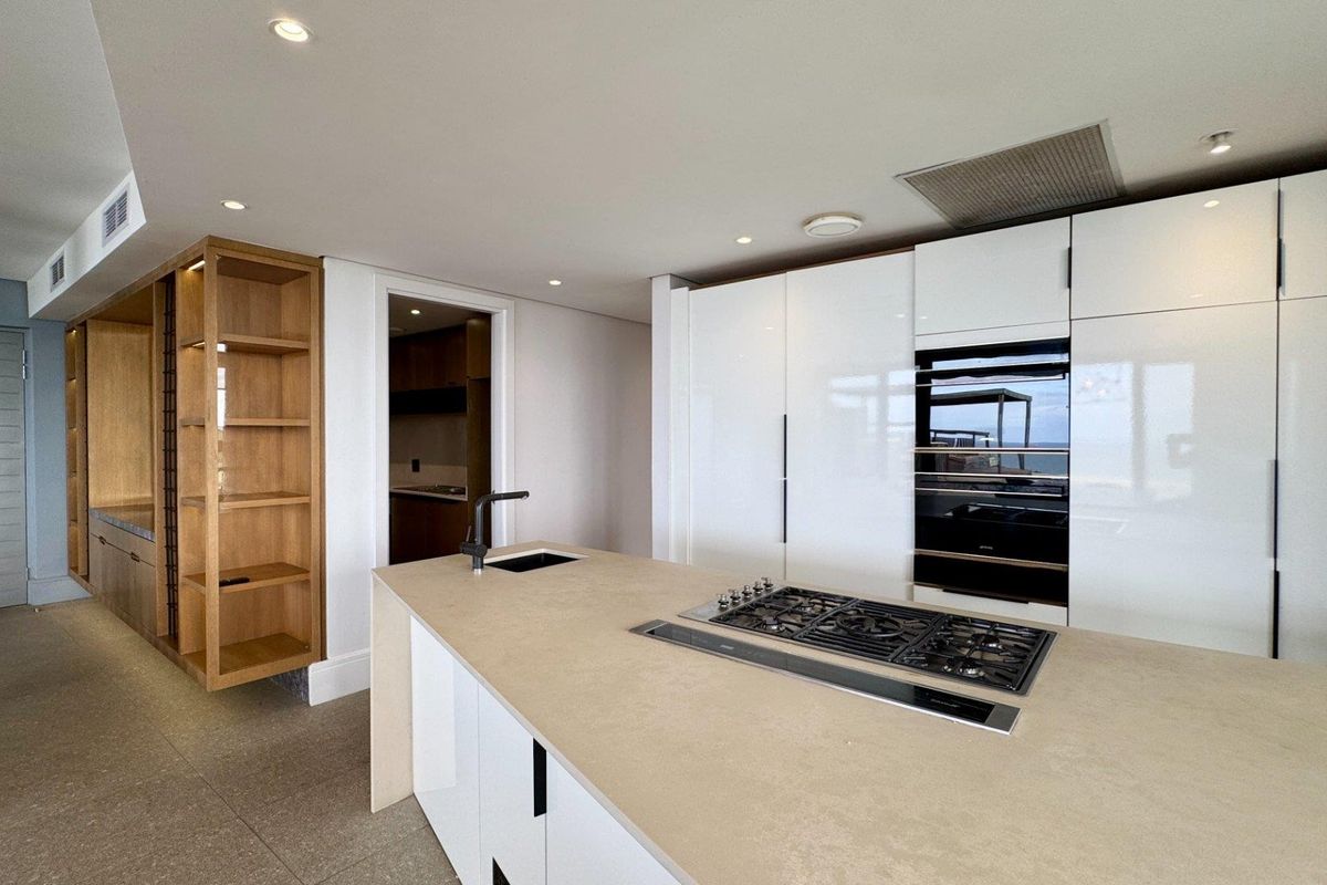 Modern kitchen featuring a central island with a gas hob, sleek white cabinetry, built-in oven, and integrated shelving in a clean, contemporary design.