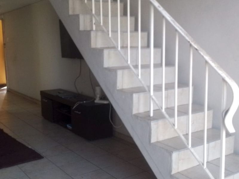 Living area featuring a central staircase with a metal balustrade and tiled flooring, showing signs of wear and dated finishes.