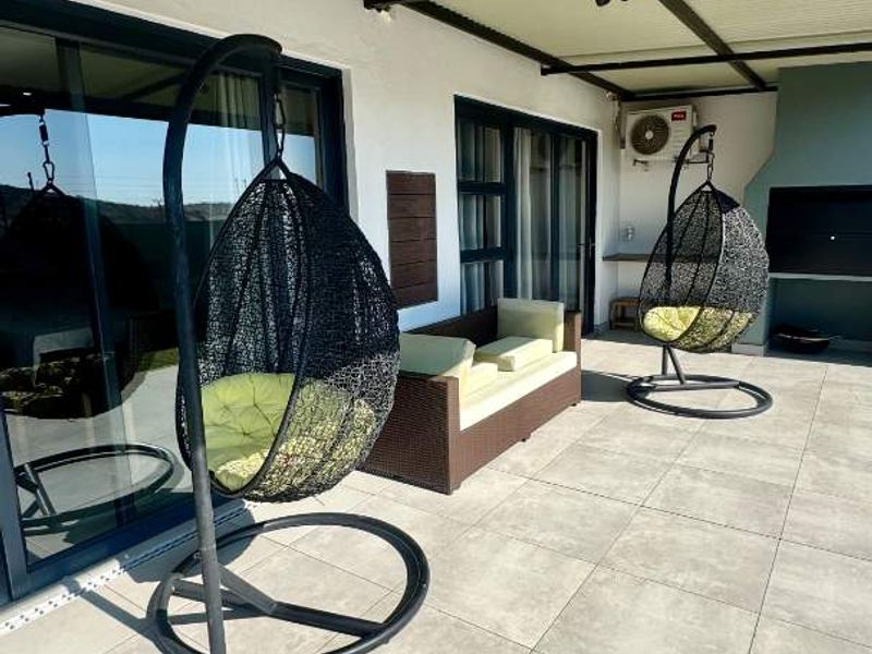 A covered patio area featuring large format floor tiles, sliding glass doors, and a built-in braai, providing a functional outdoor entertainment space.