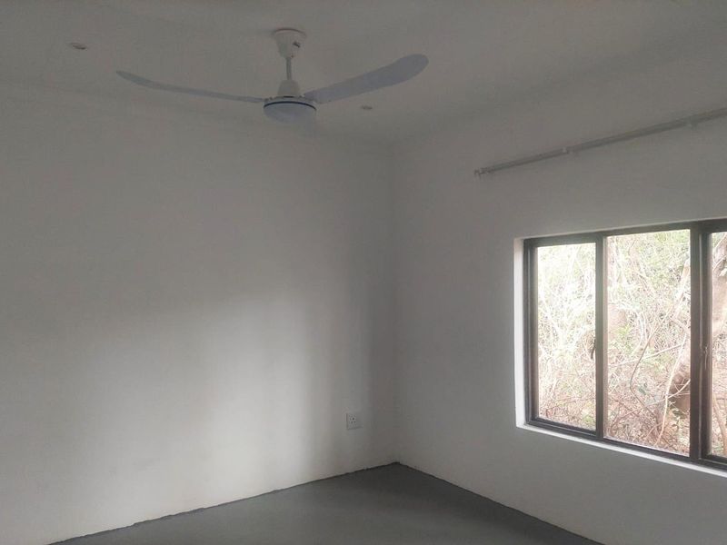 A clean, empty bedroom featuring a ceiling fan, sliding window with natural light, and neutral wall finishes.