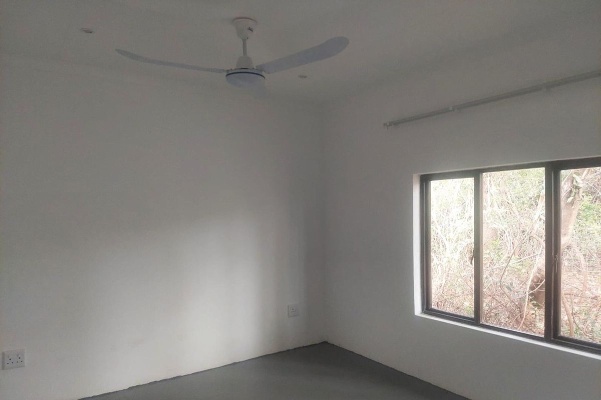 A clean, empty bedroom featuring a ceiling fan, sliding window with natural light, and neutral wall finishes.