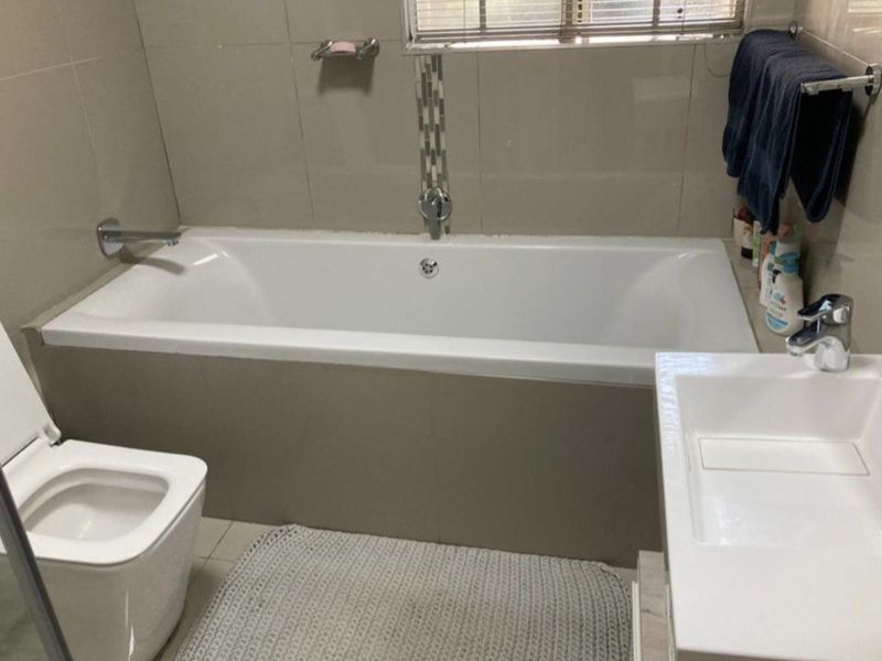 A functional bathroom featuring a built-in bathtub, modern toilet, and a vanity basin with tiled wall finishes.
