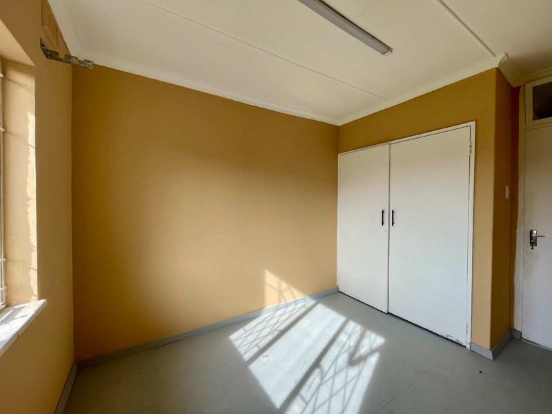 An empty bedroom featuring built-in cupboards, security bars on the window, and a neutral paint finish, ready for renovation or staging.
