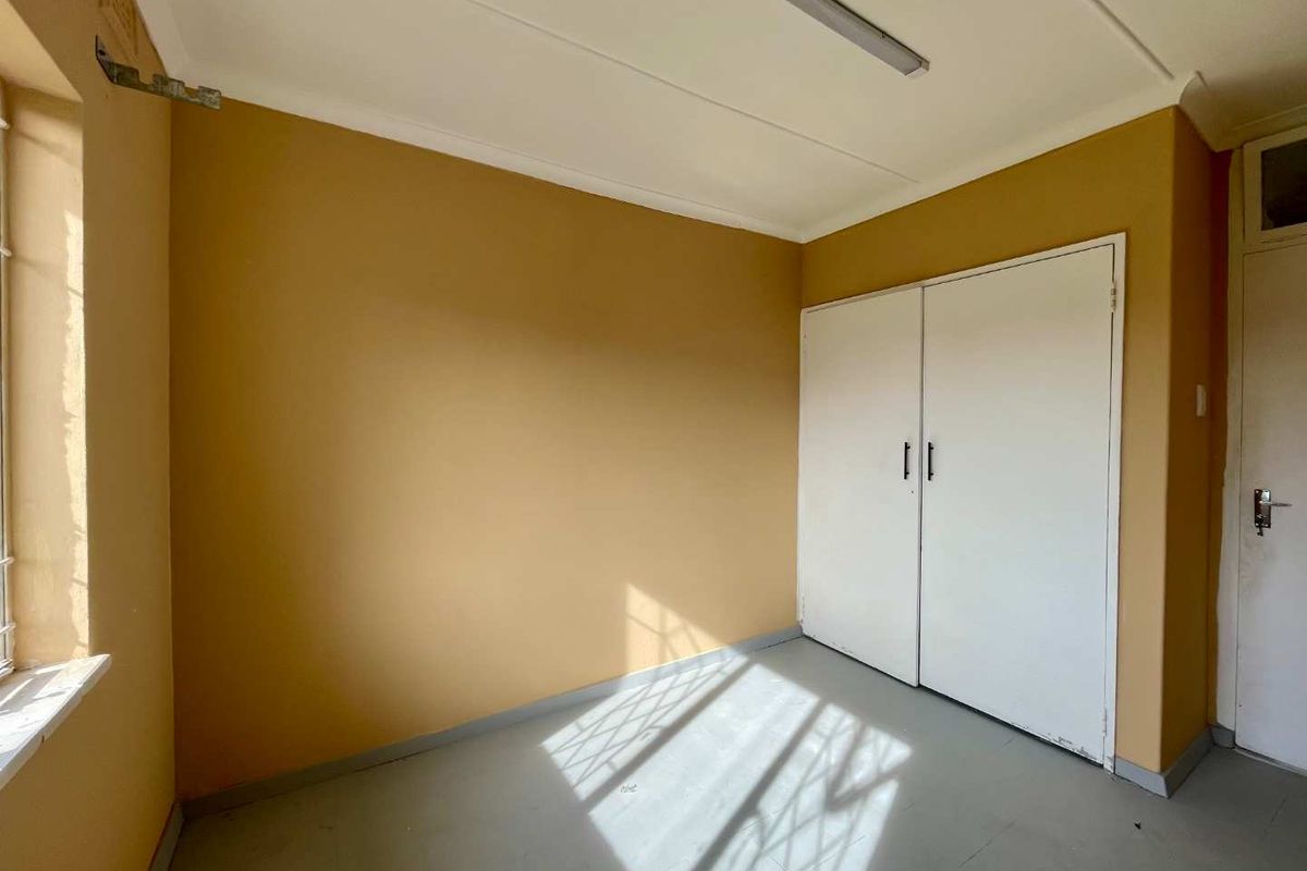 An empty bedroom featuring built-in cupboards, security bars on the window, and a neutral paint finish, ready for renovation or staging.