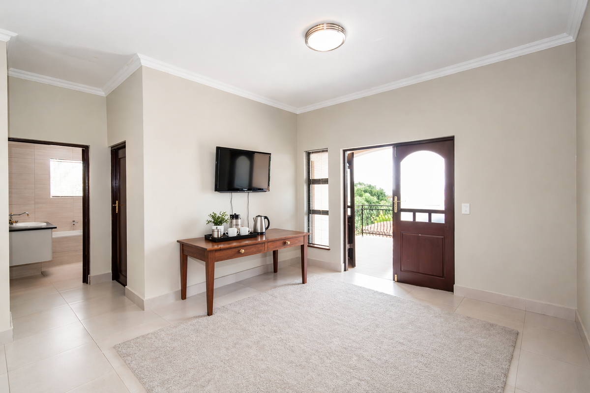 A bright bedroom featuring tiled flooring, crown molding, and direct access to a private balcony, with an adjoining en-suite bathroom.
