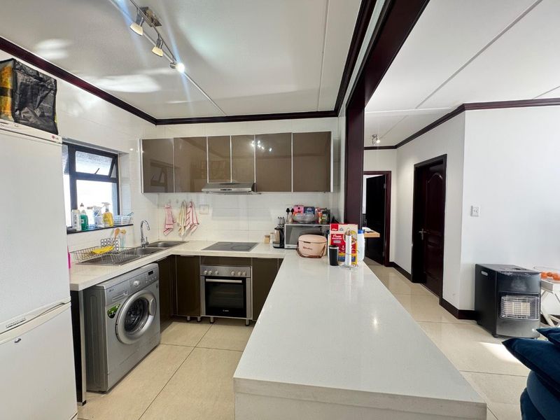 Modern kitchen featuring sleek brown cabinetry, stone countertops, a breakfast bar, and integrated appliances including an oven and hob.