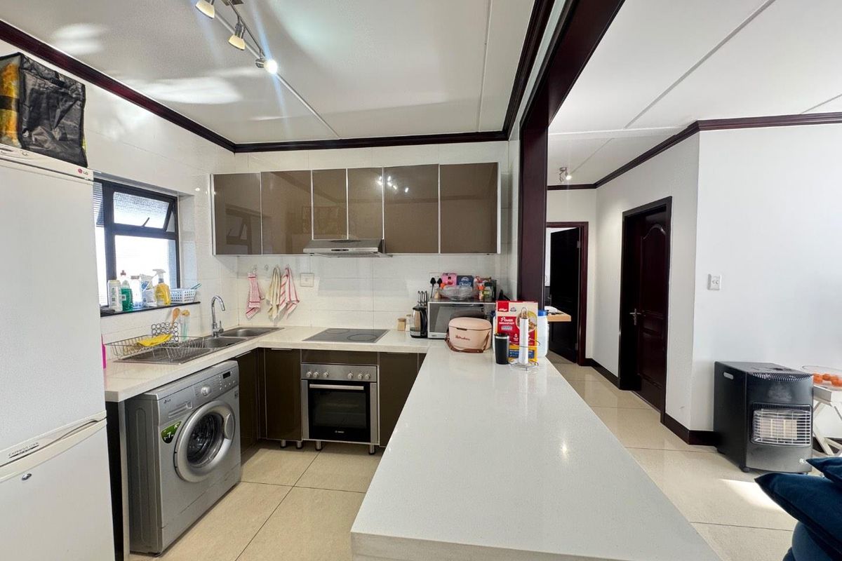 Modern kitchen featuring sleek brown cabinetry, stone countertops, a breakfast bar, and integrated appliances including an oven and hob.