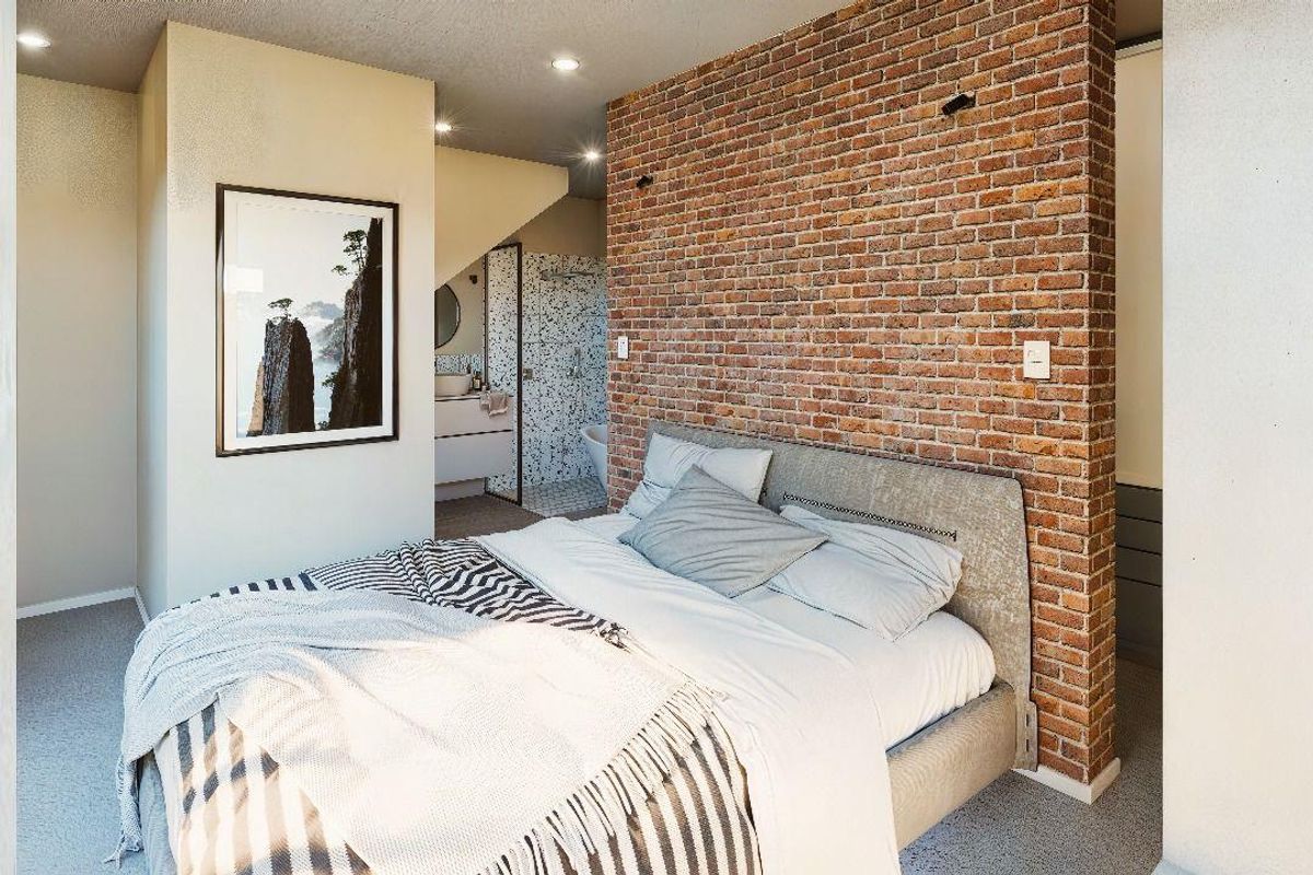 A modern bedroom featuring an exposed brick feature wall, recessed ceiling lighting, and an open-plan layout leading to an en-suite bathroom.