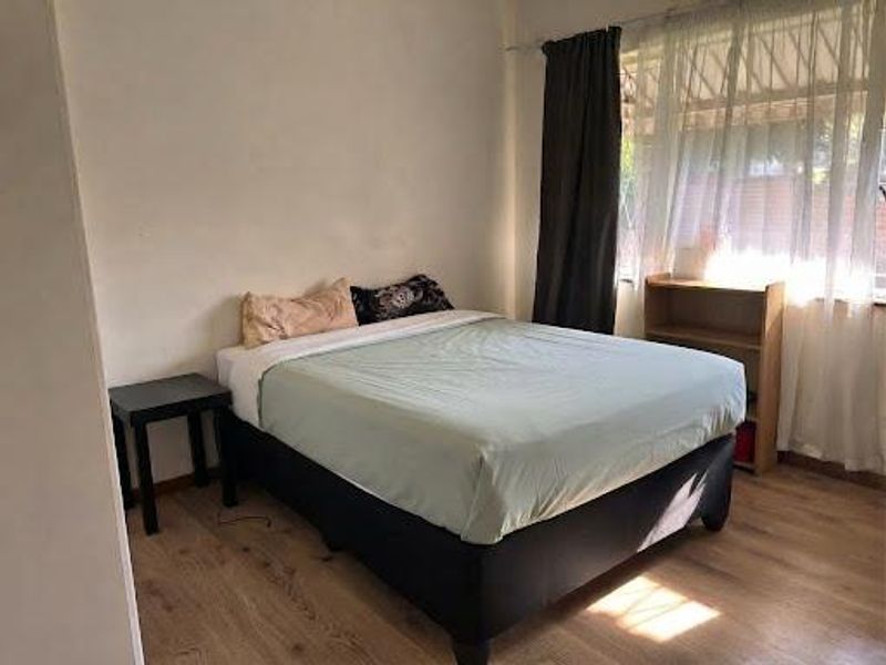 A standard bedroom featuring laminate flooring and large windows with curtain rails, providing natural light.