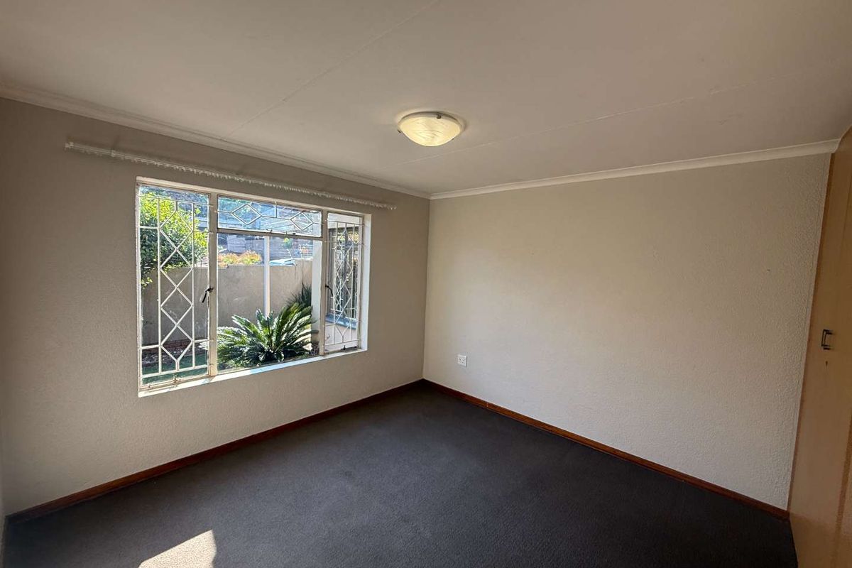 A vacant bedroom featuring carpeted flooring, a built-in cupboard, and a window fitted with security bars, offering a clean and neutral space.