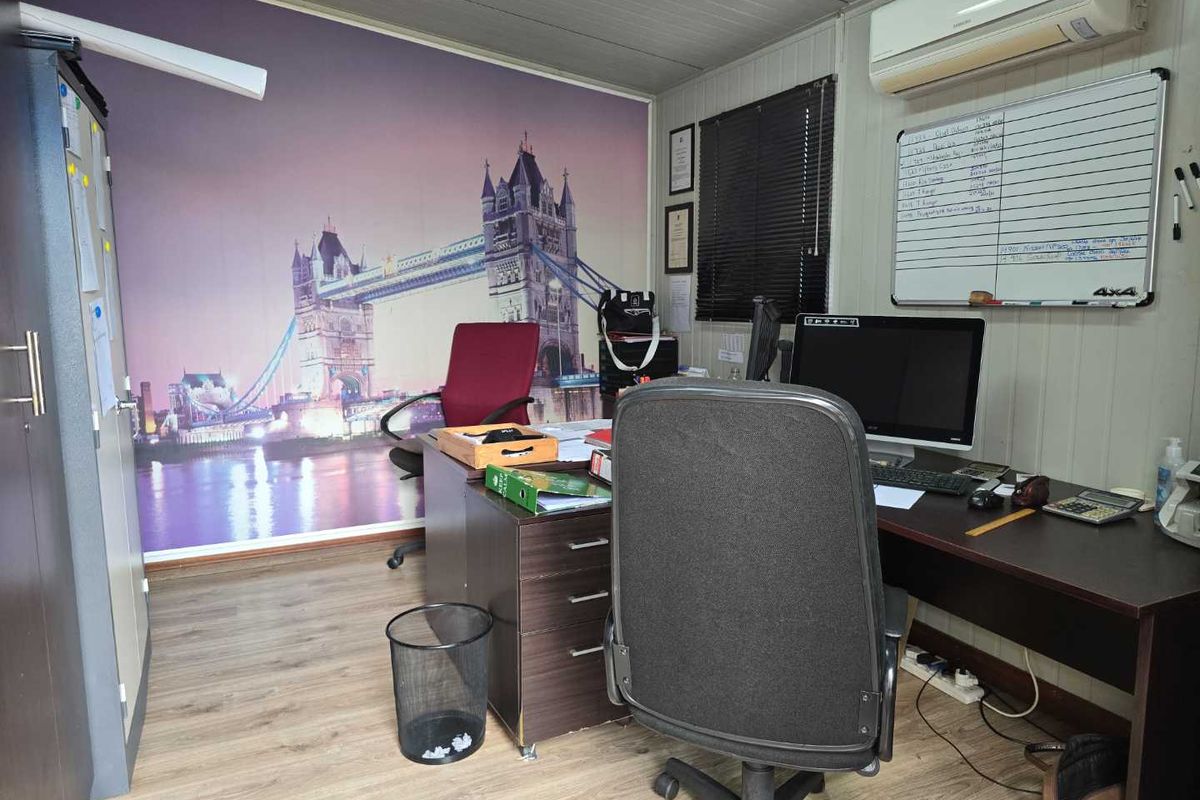 A functional office space featuring laminate flooring, a wall-mounted air conditioning unit, and venetian blinds, suitable for a professional work environment.