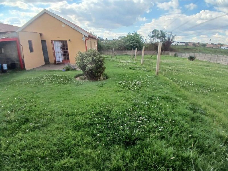 A rear view of the property showing a large, grassed backyard area with a concrete perimeter wall and security gate access.