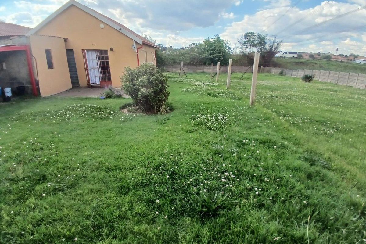 A rear view of the property showing a large, grassed backyard area with a concrete perimeter wall and security gate access.