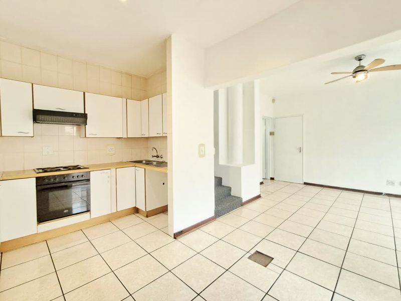 Open-plan kitchen and living area featuring tiled flooring, built-in cabinetry, and an integrated oven and hob, leading to a staircase.