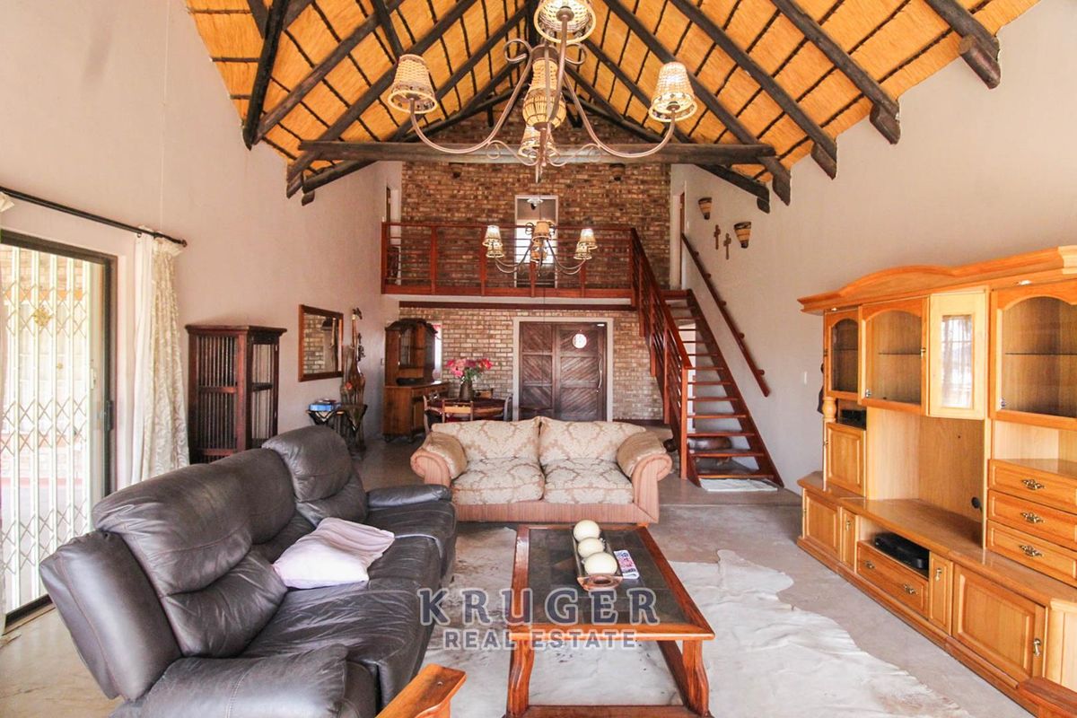 Spacious living area featuring a high vaulted thatch ceiling with exposed timber trusses, a brick feature wall, and a mezzanine level with a timber staircase.