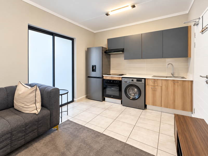 Modern open-plan kitchen and living area featuring contemporary cabinetry, integrated appliances, tiled flooring, and direct access to an outdoor space via sliding doors.