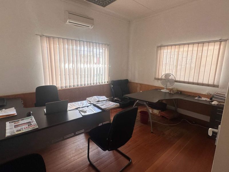 A functional office space featuring timber flooring, wall paneling, vertical blinds, and a wall-mounted air conditioning unit.