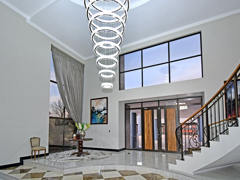 Grand double-volume entrance hall featuring a striking modern chandelier, elegant wrought iron staircase, and expansive windows providing abundant natural light.