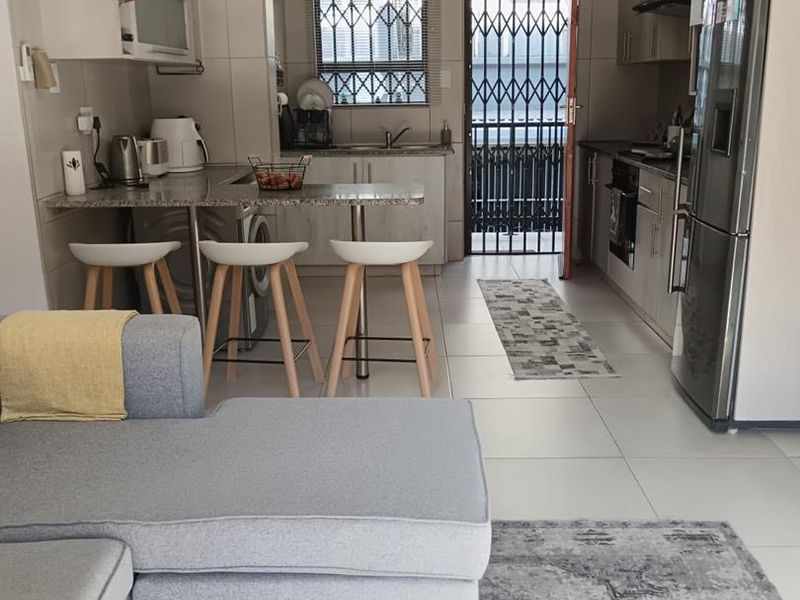 Open-plan kitchen and living area featuring modern cabinetry, granite countertops, built-in appliances, and tiled flooring with direct access to an exterior security gate.