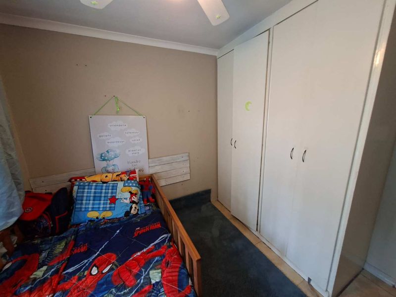 A bedroom featuring built-in cupboards and a ceiling fan, currently showing signs of wear on the walls and flooring.