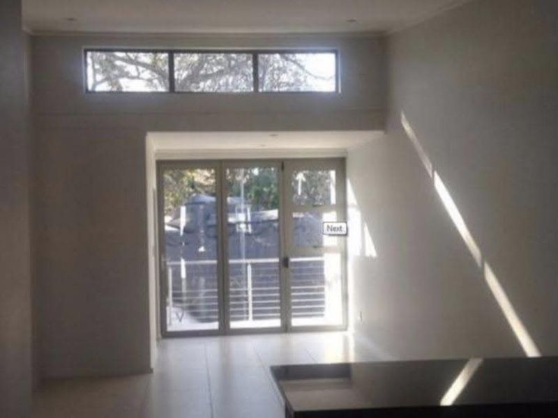 An open-plan living area featuring tiled floors, recessed lighting, and large glass doors leading to a balcony, with a modern granite countertop visible.