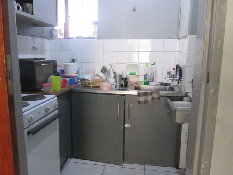 A compact kitchen featuring a stainless steel sink, tiled backsplash, and built-in cabinetry, requiring some maintenance and cosmetic updates.