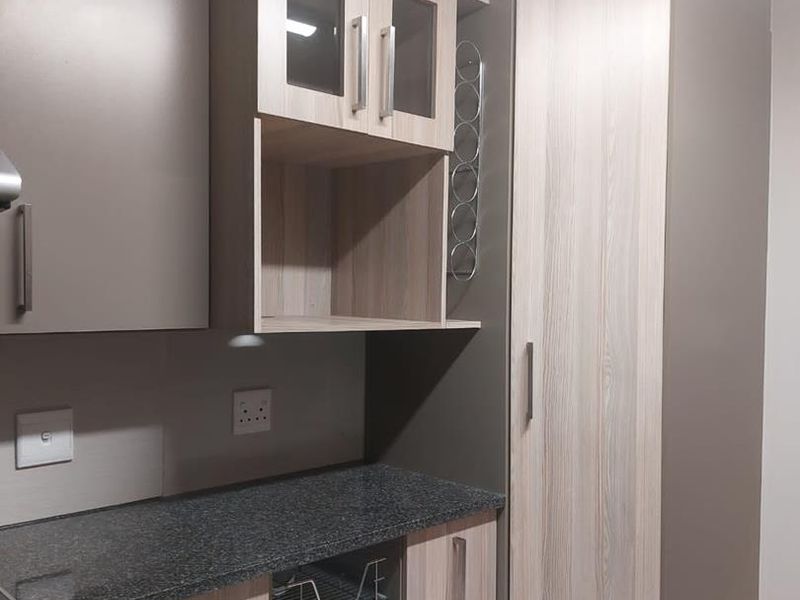 Modern kitchen area featuring granite countertops, ample built-in cabinetry, a tall pantry cupboard, and convenient pull-out wire storage baskets.