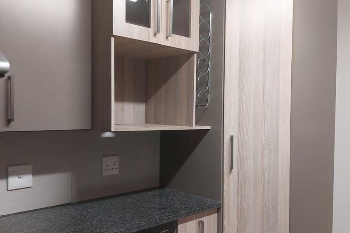 Modern kitchen area featuring granite countertops, ample built-in cabinetry, a tall pantry cupboard, and convenient pull-out wire storage baskets.