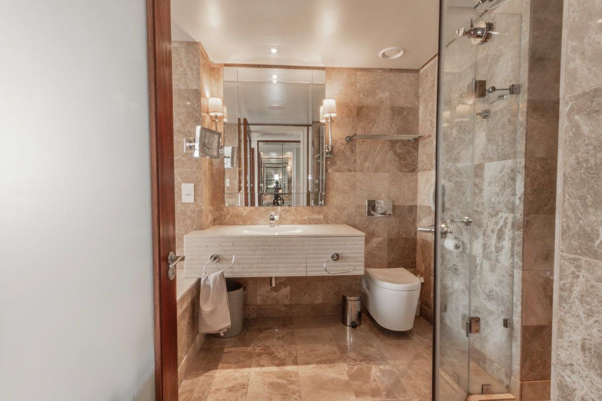 Modern bathroom featuring stone wall and floor tiling, a wall-mounted vanity with integrated basin, wall-hung toilet, and a glass-enclosed shower.