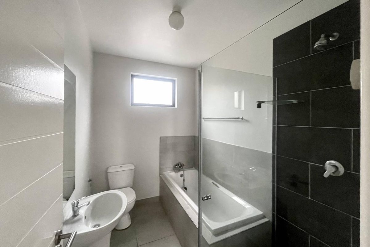 Modern bathroom featuring a white pedestal basin, toilet, and a combined bathtub and shower enclosure with dark tiled wall accents.