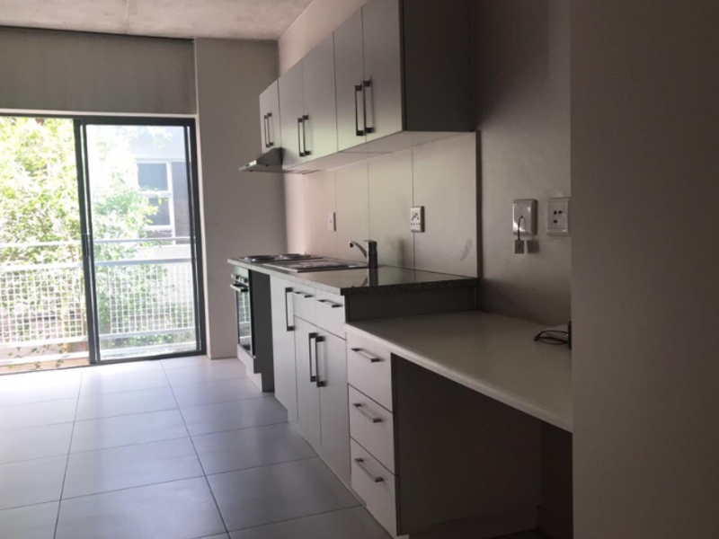 Modern kitchen featuring built-in cabinetry, granite countertops, integrated oven and hob, and tiled flooring with direct access to a balcony.