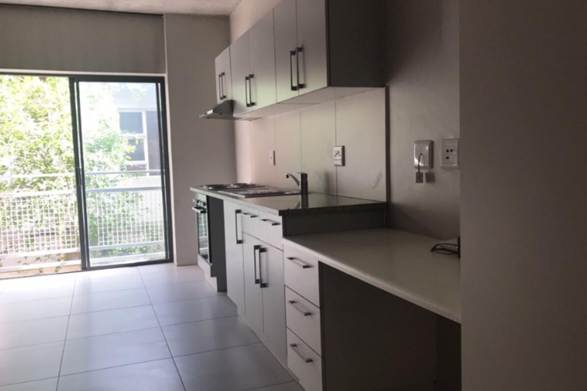 Modern kitchen featuring built-in cabinetry, granite countertops, integrated oven and hob, and tiled flooring with direct access to a balcony.