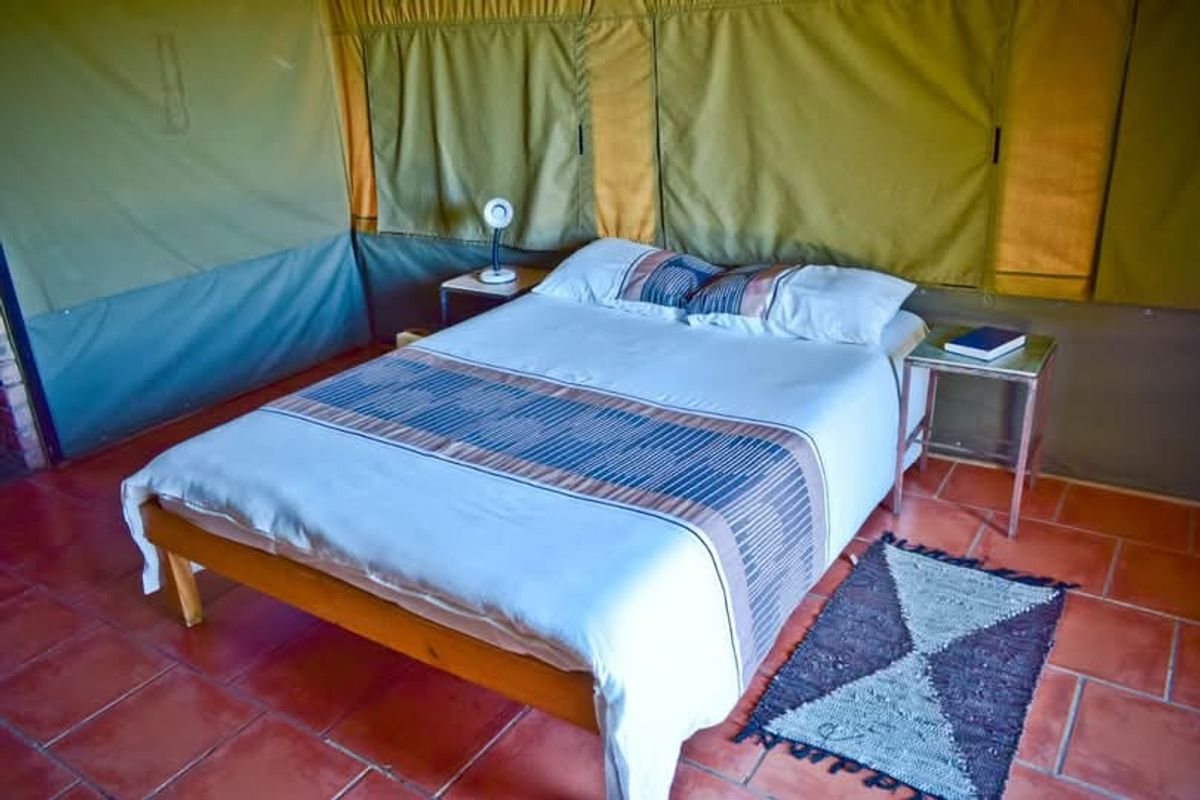 A bedroom within a lodge tent featuring terracotta tile flooring and canvas walls, providing a rustic and authentic safari-style accommodation experience.